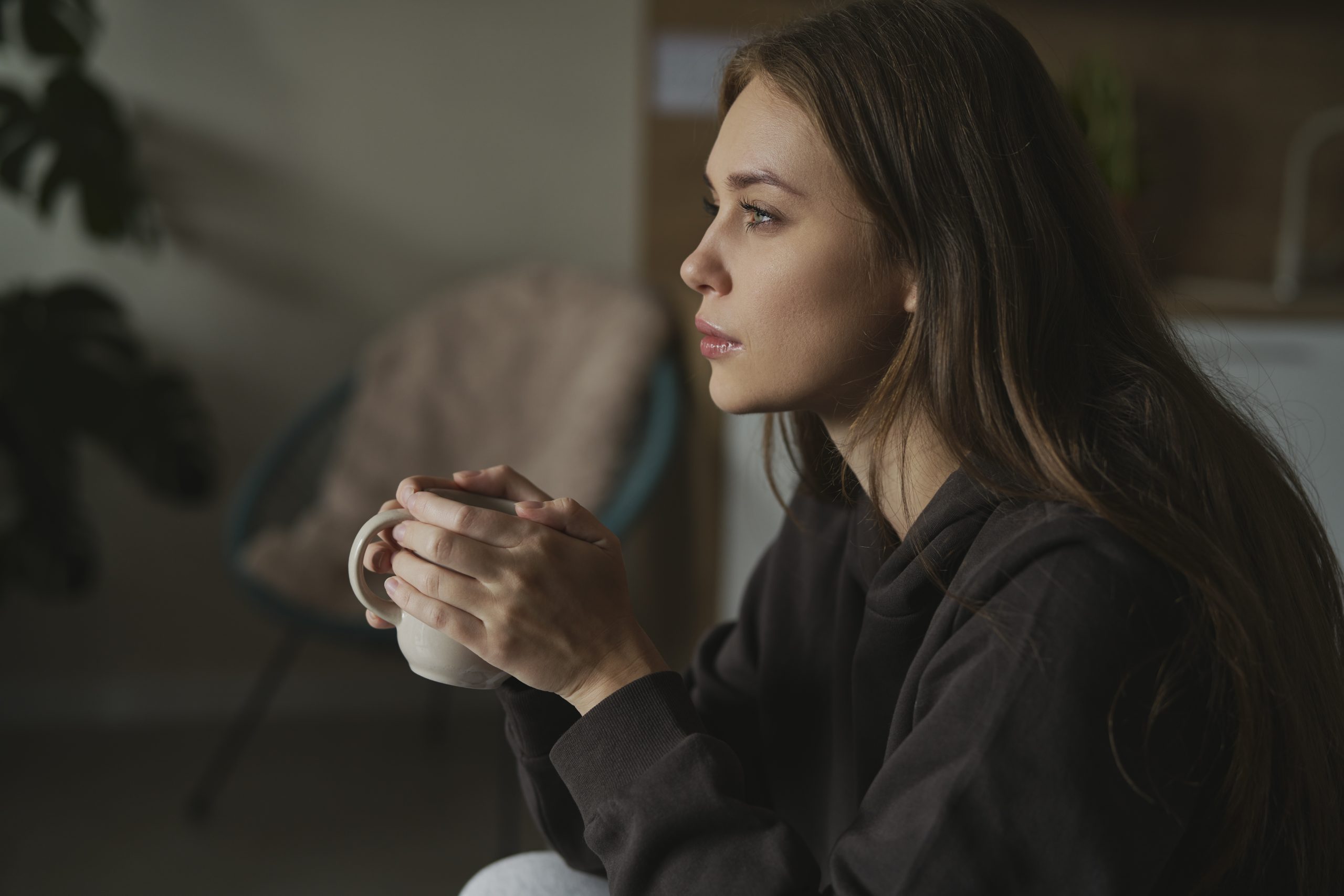 Woman with distant gaze holding a mug, quietly experiencing high functioning depression